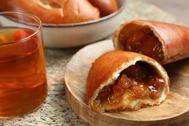 Photo of Delicious baked patties with jam and tea on wicker mat, closeup