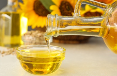 Photo of Pouring sunflower oil from jug into bowl on white  table, closeup