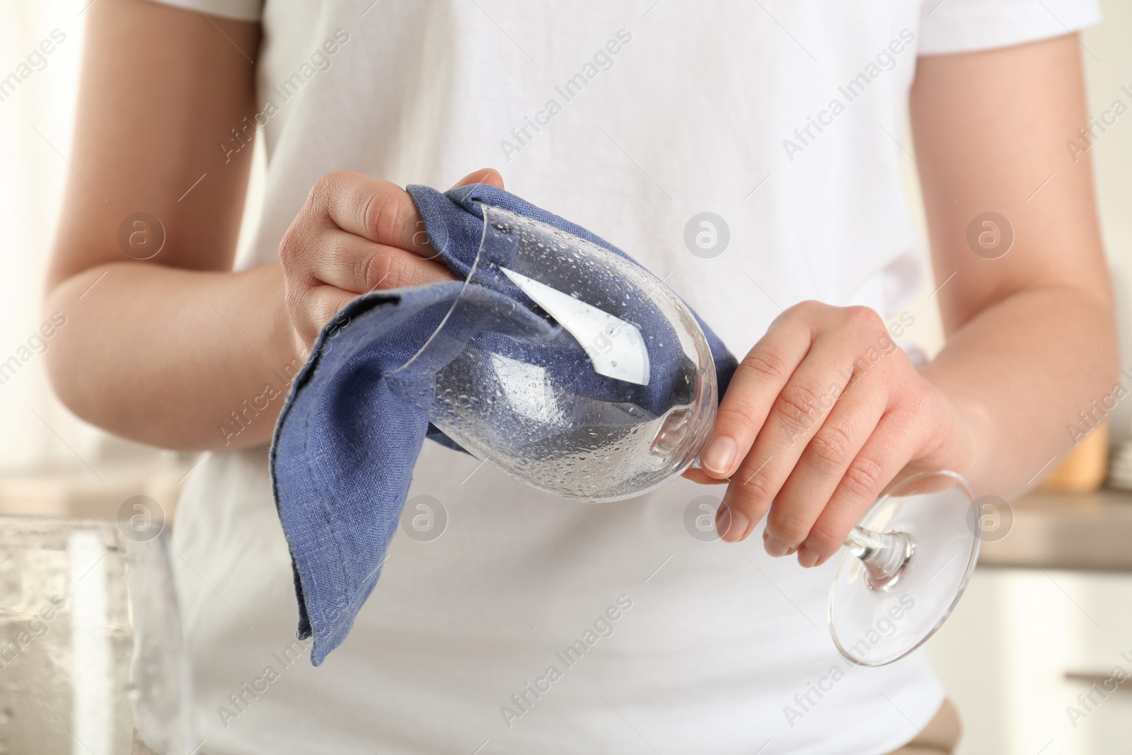 Photo of Woman wiping glass with blue towel in kitchen, closeup