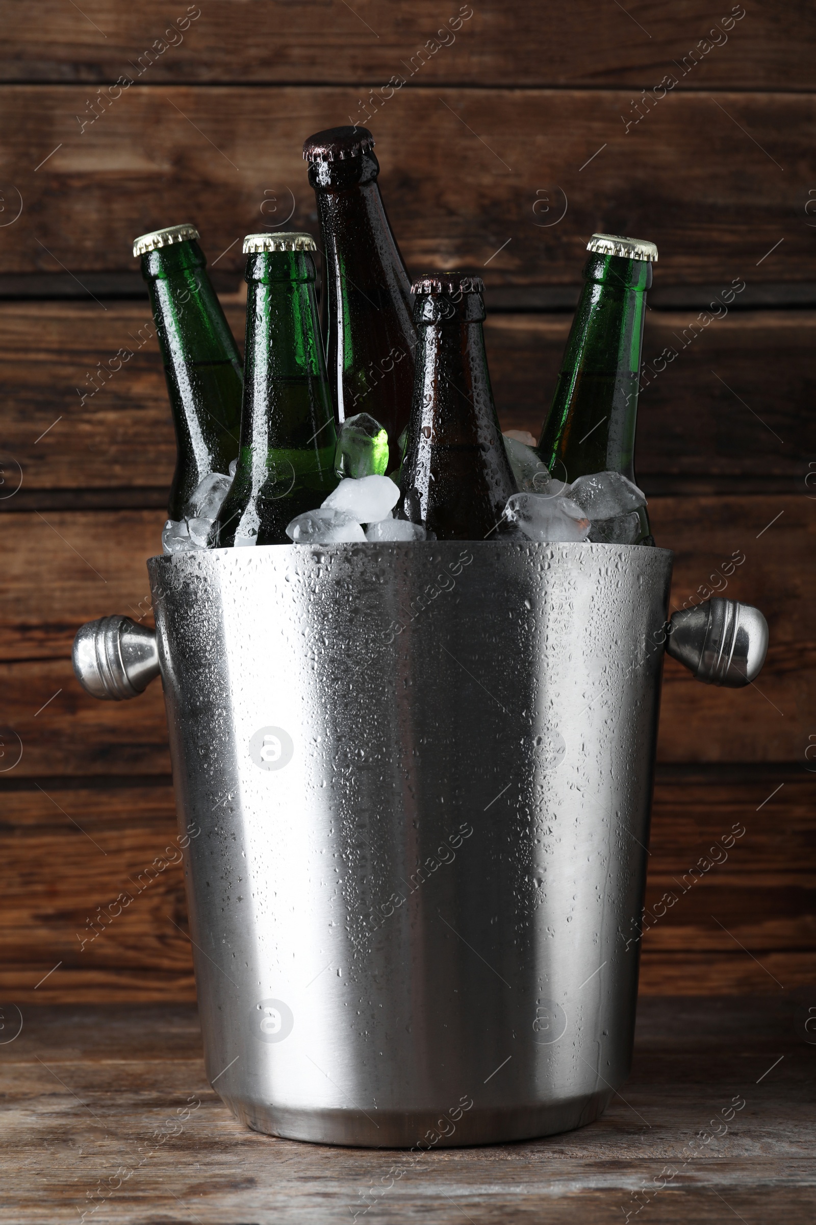 Photo of Metal bucket with bottles of beer and ice cubes on wooden table