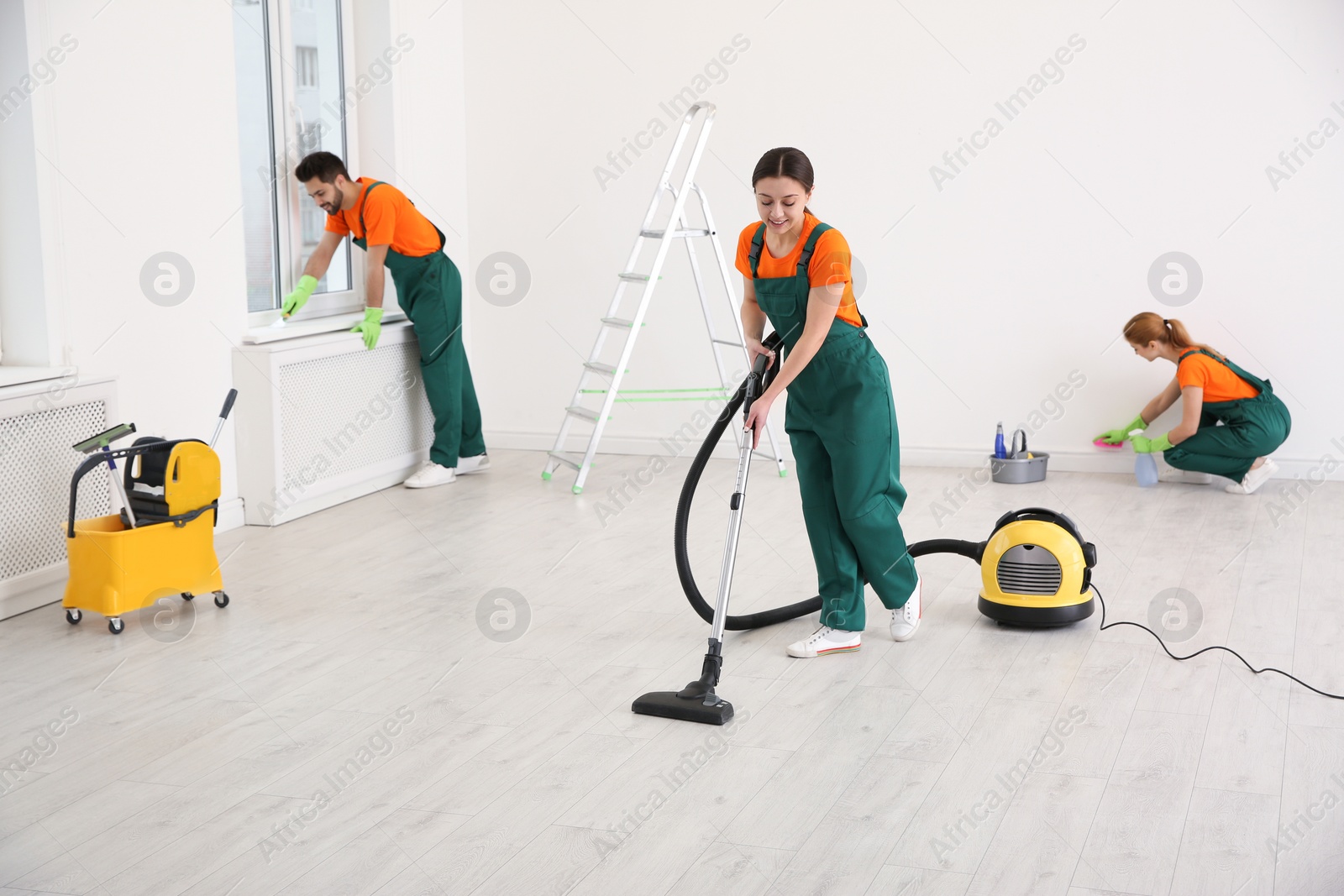 Photo of Team of professional janitors in uniforms cleaning room