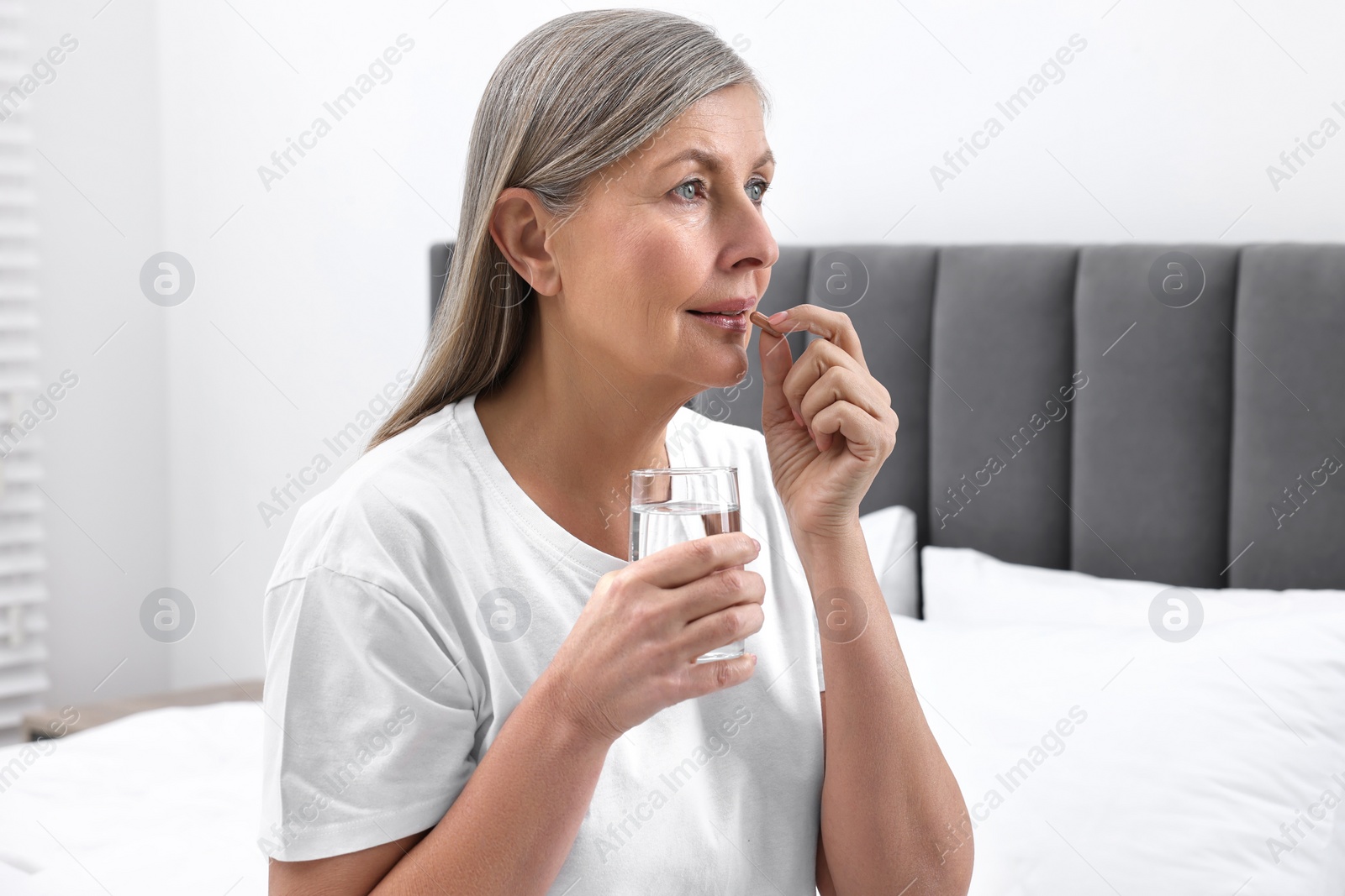 Photo of Beautiful woman taking vitamin pill in bedroom