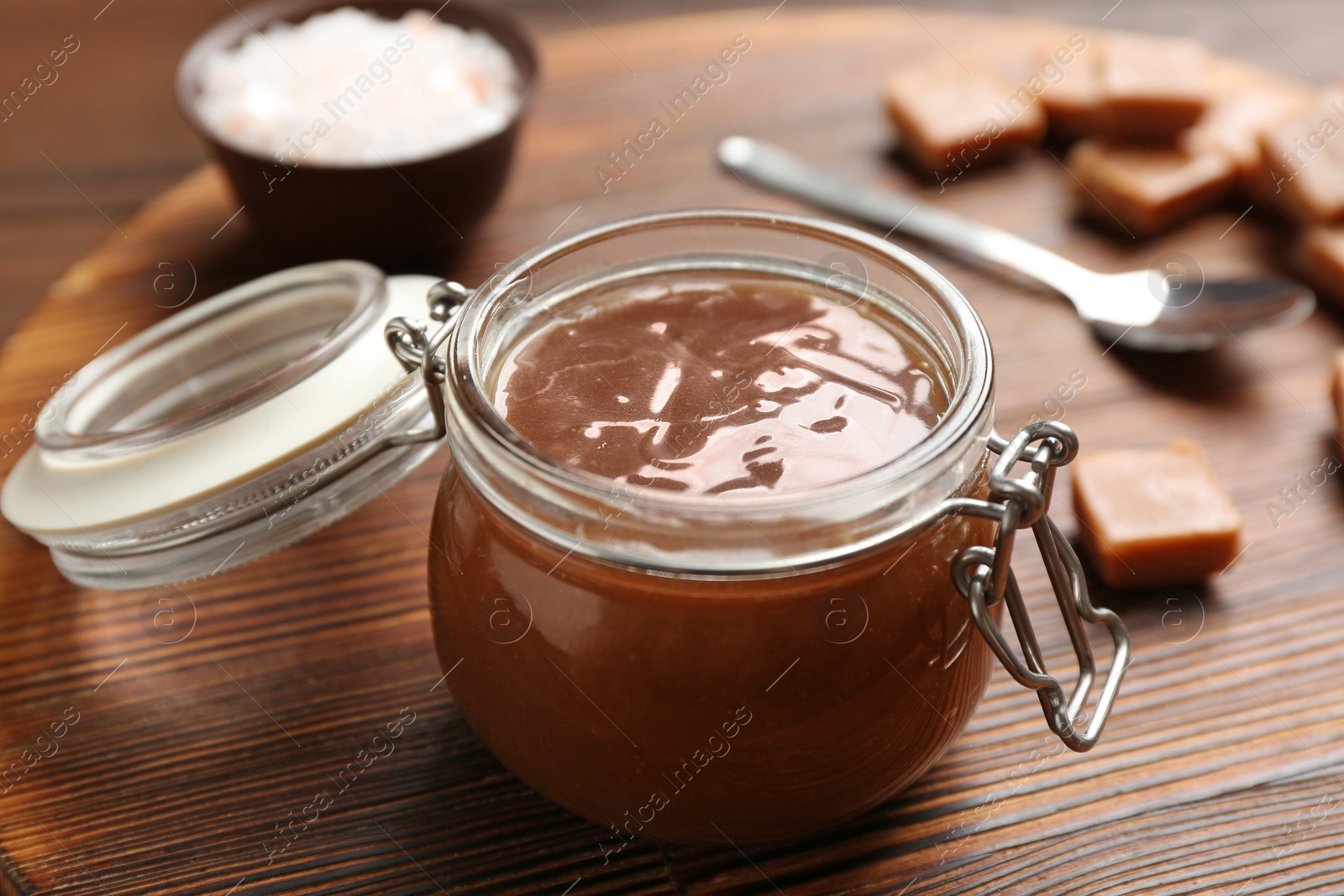 Photo of Jar of tasty caramel sauce on board, closeup