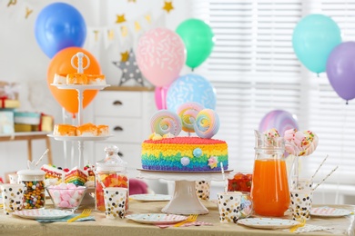 Photo of Bright birthday cake and other treats on table in decorated room