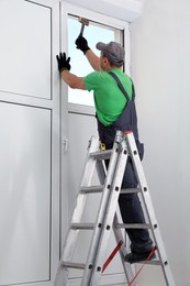 Worker on folding ladder installing window indoors