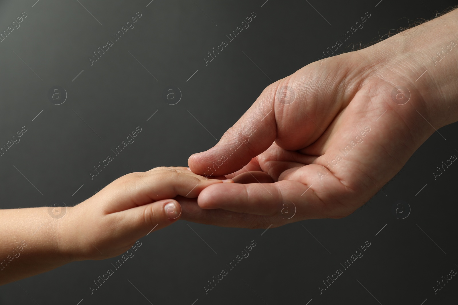 Photo of Father and child holding hands on dark grey background, closeup