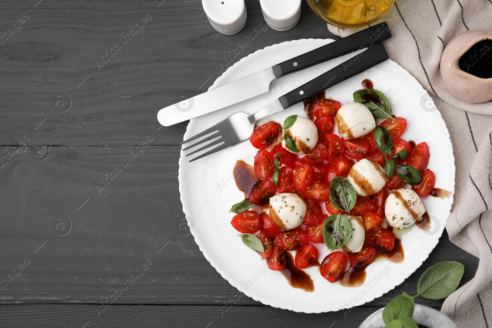 Photo of Tasty salad Caprese with tomatoes, mozzarella balls, basil served on grey wooden table, flat lay. Space for text
