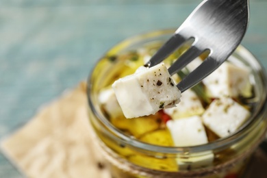 Fork with pickled feta cheese over jar on blue table, closeup