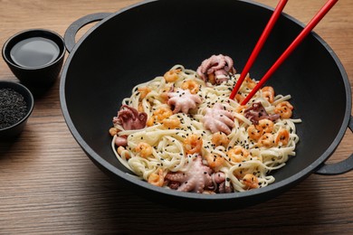 Photo of Stir fried noodles with seafood in wok on wooden table