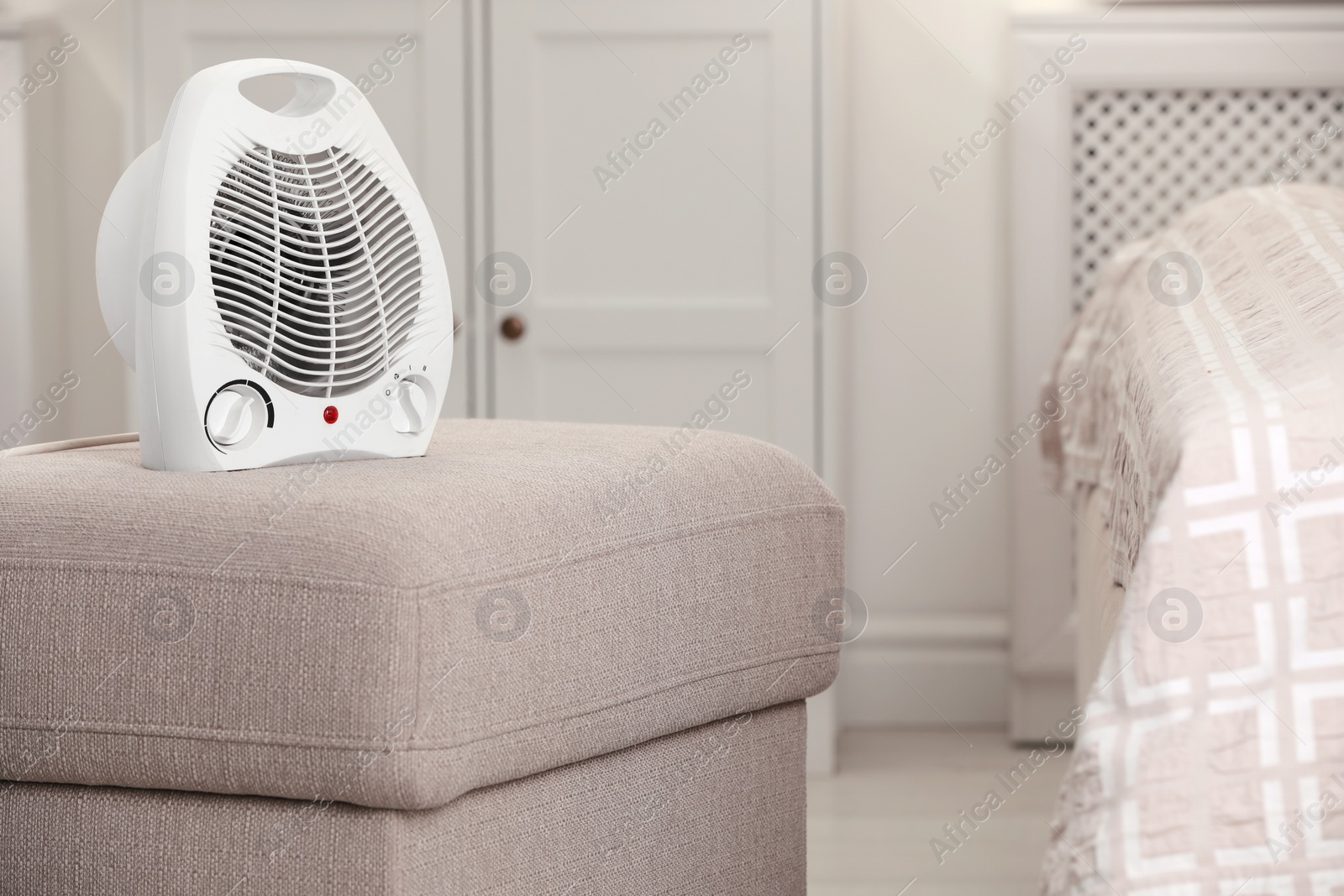 Photo of Modern electric fan heater on pouf in cozy room