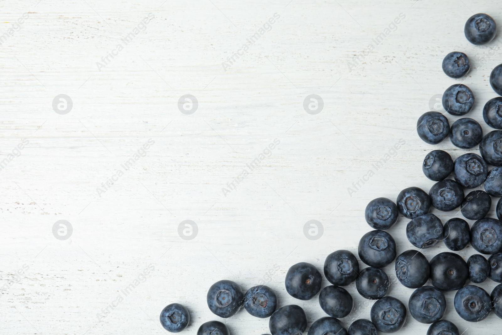 Photo of Tasty fresh blueberries on white wooden table, top view with space for text