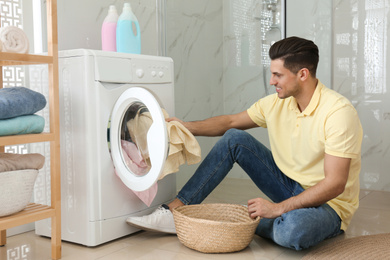 Man putting clothes into washing machine in bathroom. Laundry day