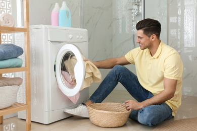 Photo of Man putting clothes into washing machine in bathroom. Laundry day