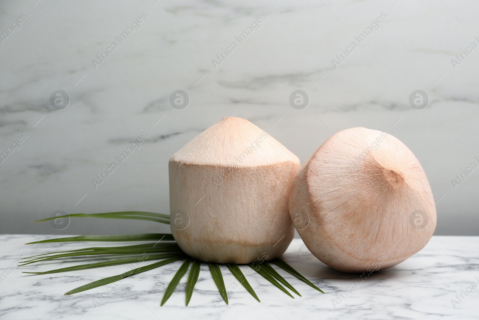 Photo of Young peeled coconuts with palm leaf on white marble table