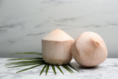 Photo of Young peeled coconuts with palm leaf on white marble table