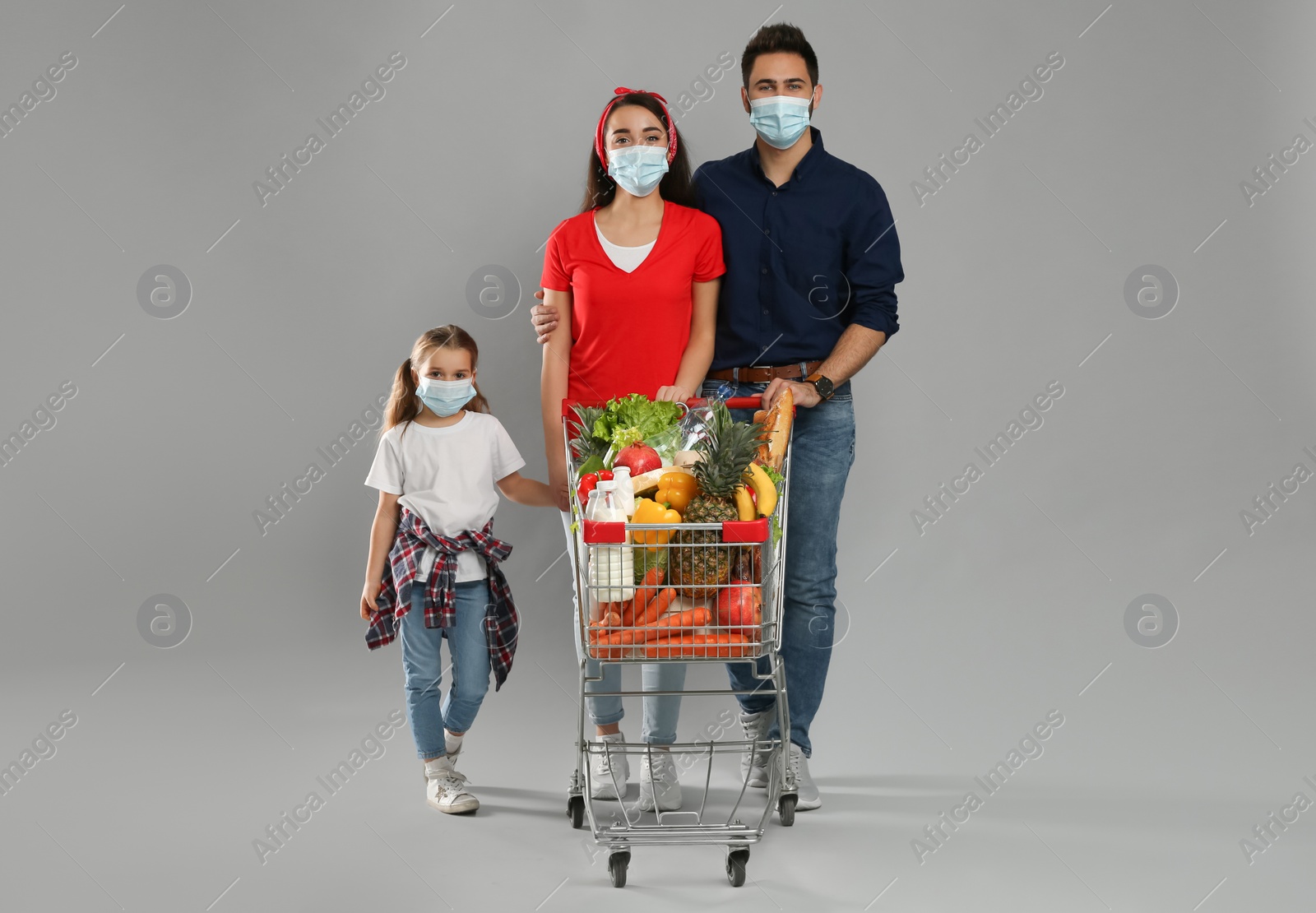 Photo of Family in medical masks with shopping cart full of groceries on light grey background