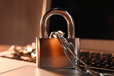 Photo of Cyber security. Laptop with padlock and chain on table, closeup