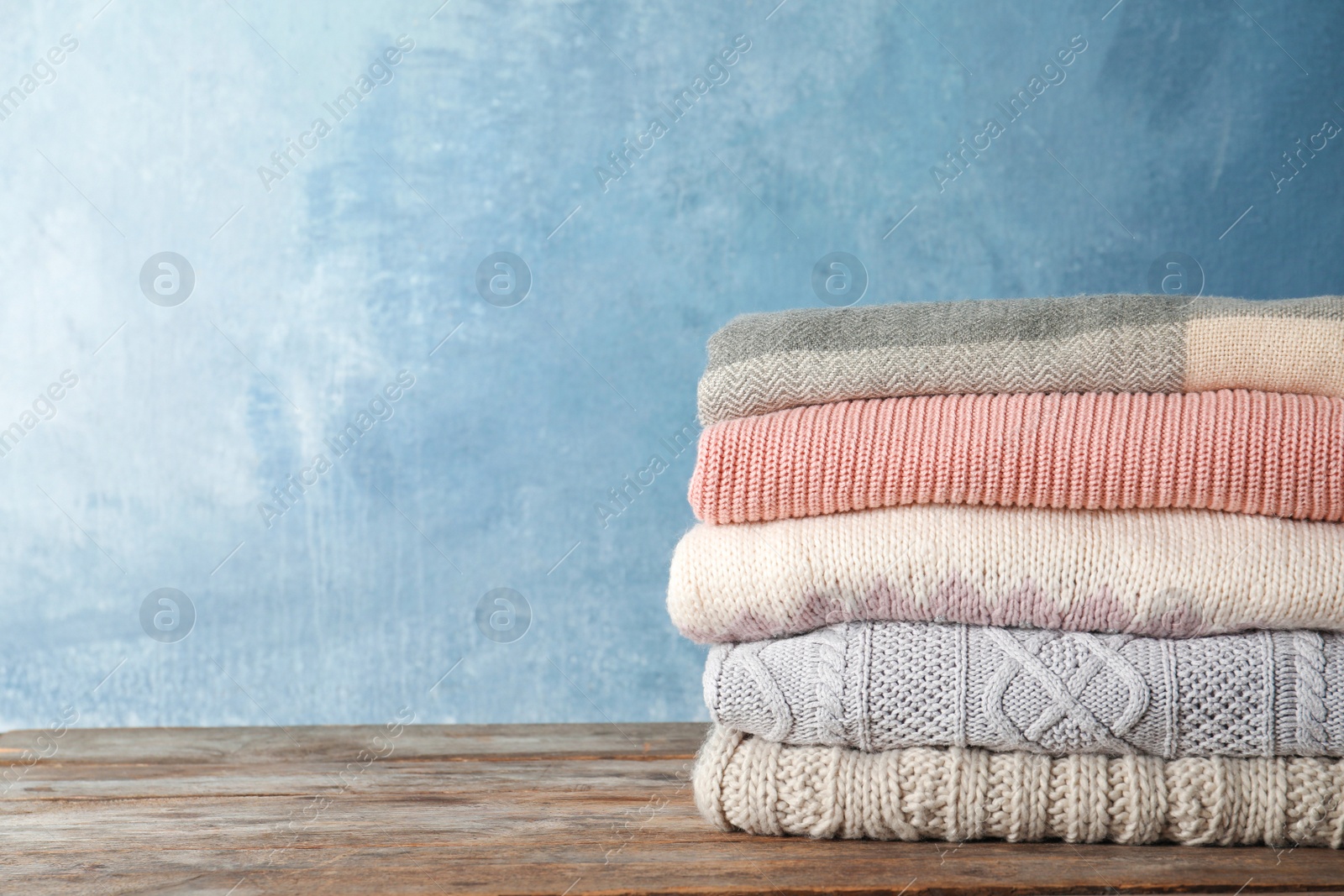 Photo of Stack of warm autumn clothes on wooden table. Space for text