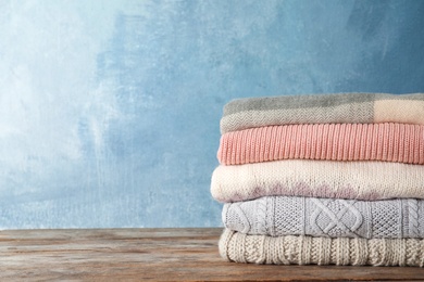 Photo of Stack of warm autumn clothes on wooden table. Space for text