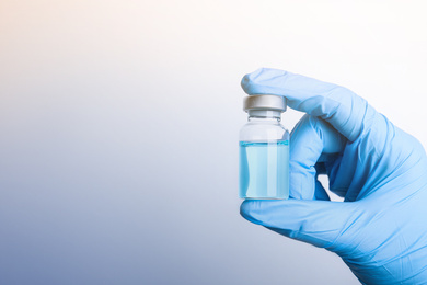 Image of Doctor holding vial with medication on light background, closeup view and space for text. Vaccination and immunization