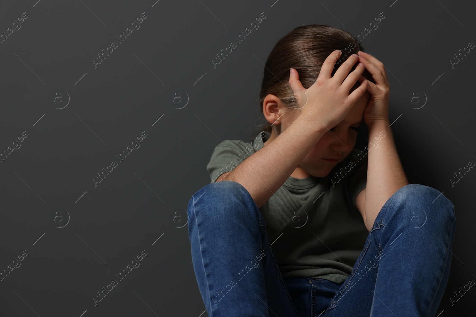 Photo of Child abuse. Upset girl sitting on floor near grey wall, space for text