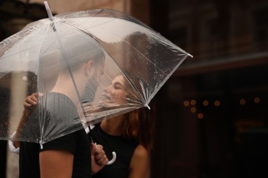 Young couple with umbrella enjoying time together under rain on city street, space for text