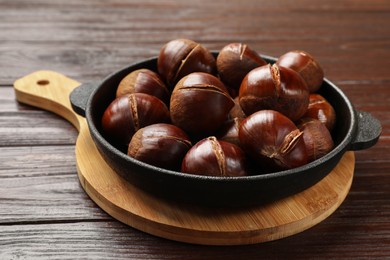 Photo of Roasted edible sweet chestnuts in baking dish on wooden table, closeup