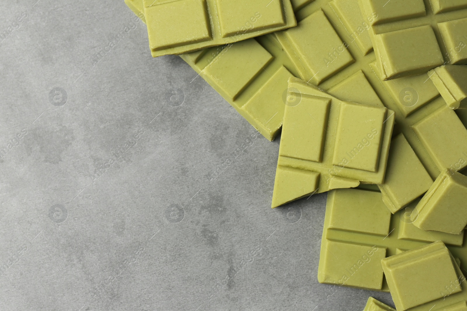 Photo of Pieces of tasty matcha chocolate bars on grey textured table, top view. Space for text