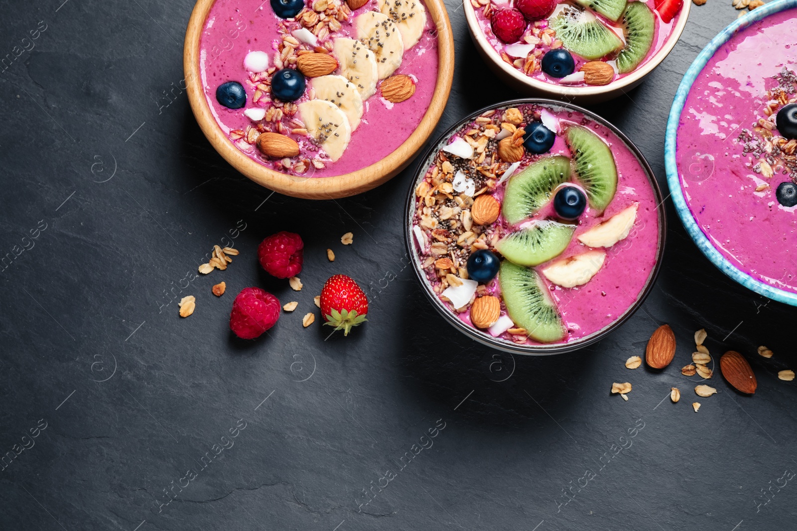 Photo of Acai smoothie bowls with granola and fruits on black table, flat lay