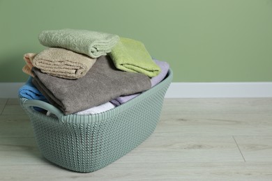 Photo of Plastic laundry basket with clean terry towels on floor near light green wall. Space for text
