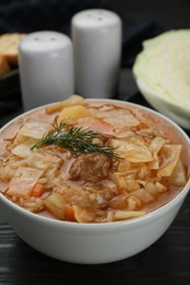 Photo of Tasty cabbage soup with meat, carrot and dill on black wooden table, closeup