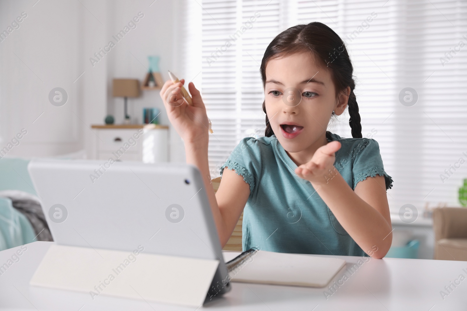 Photo of Emotional girl doing homework with tablet at table in room