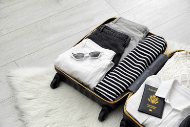 Open suitcase with clothes, passport and sunglasses on floor