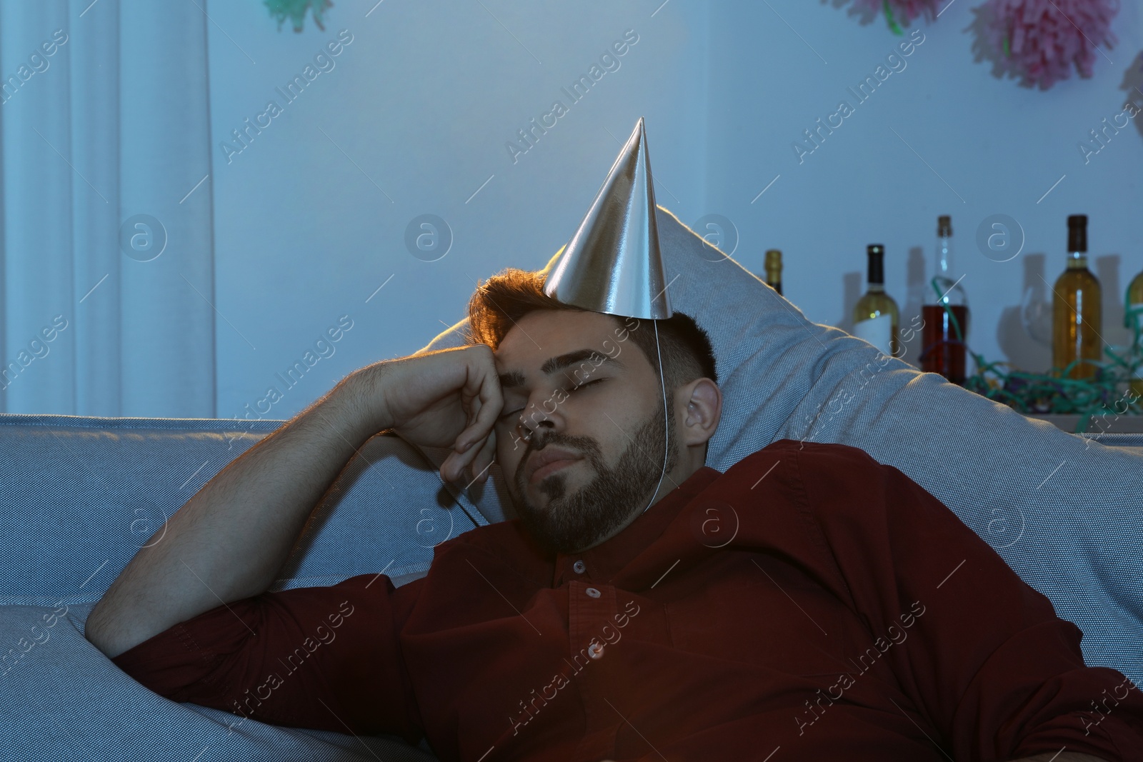 Photo of Young man with cap sleeping on sofa in room after party