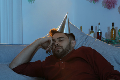 Young man with cap sleeping on sofa in room after party