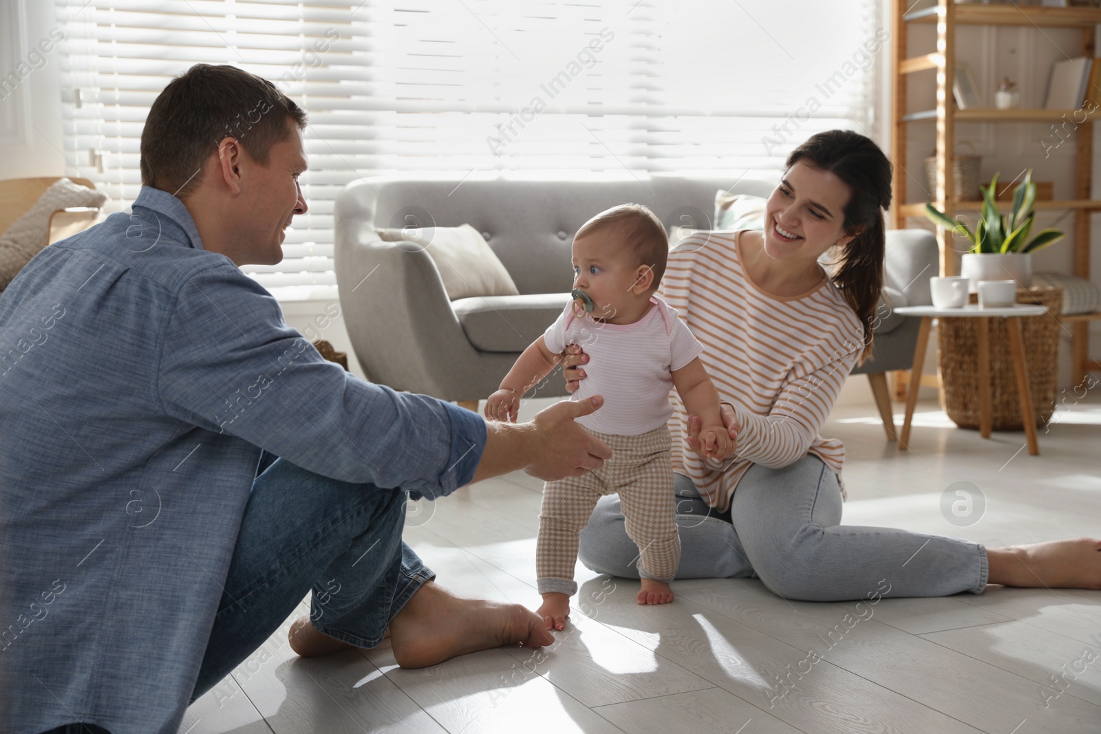 Photo of Parents supporting their baby daughter while she learning to walk at home