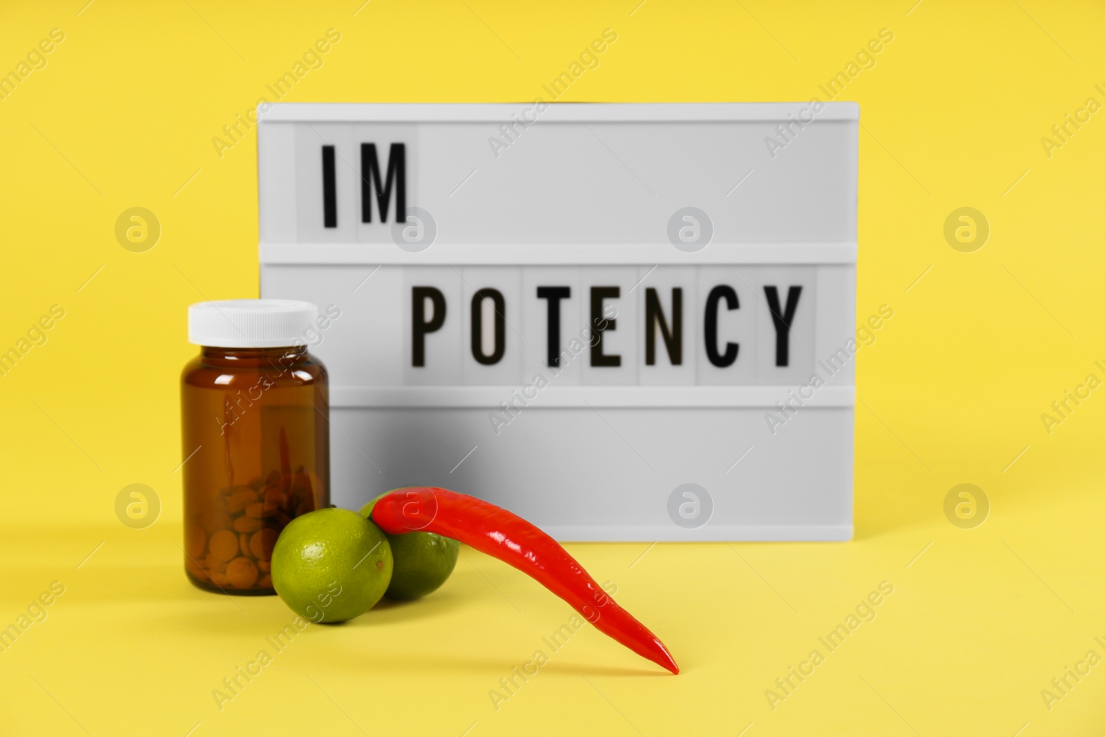 Photo of Lightbox with word IMPOTENCY, jar of pills and products symbolizing male sexual organ on yellow background