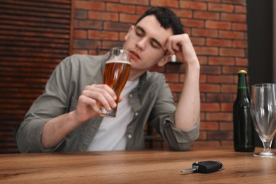 Man holding glass of alcoholic drink and sitting at table with car keys, selective focus. Don't drink and drive concept