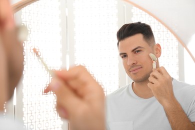 Man using mineral facial roller near mirror in bathroom