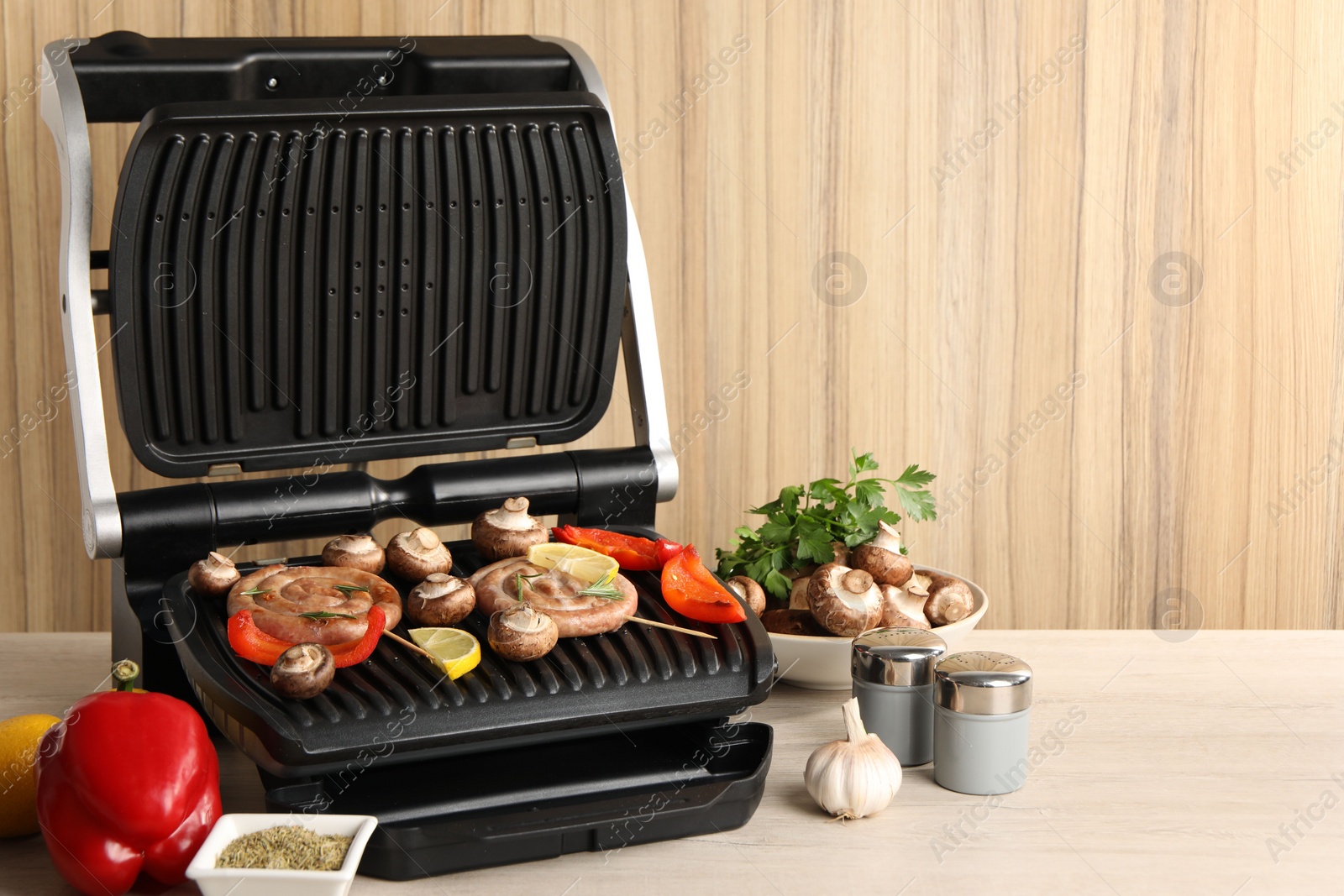 Photo of Electric grill with homemade sausages, vegetables and spices on wooden table