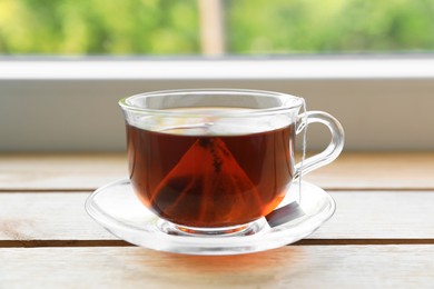 Photo of Bag of black tea in cup with hot water on wooden table indoors