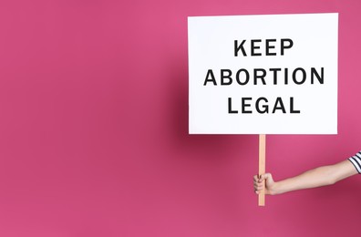 Woman holding placard with phrase Keep Abortion Legal on pink background, closeup. Abortion protest