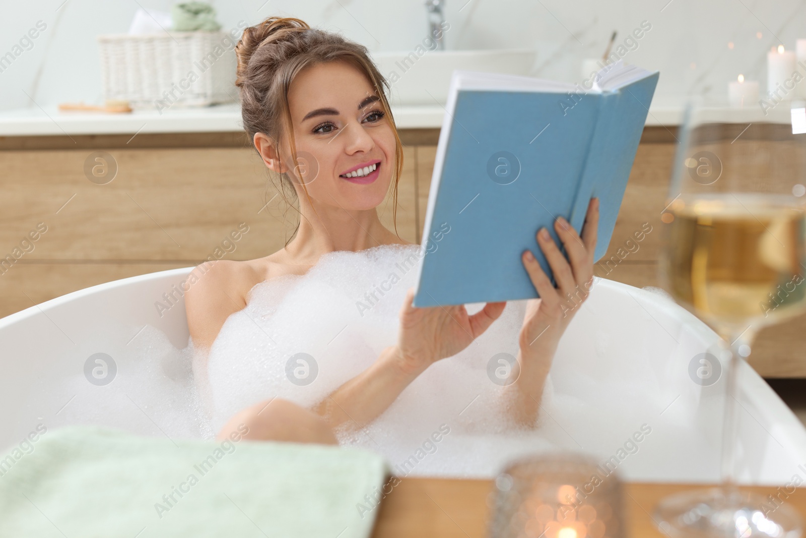 Photo of Beautiful woman reading book while enjoying bubble bath at home