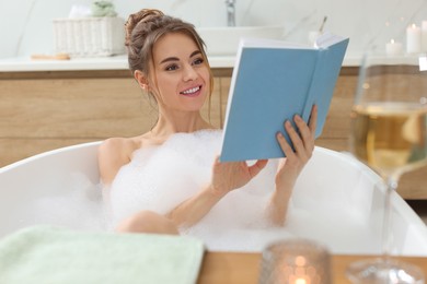 Beautiful woman reading book while enjoying bubble bath at home