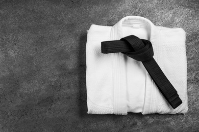 Photo of Black karate belt and white kimono on gray textured background, top view. Space for text