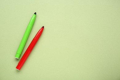 Colorful markers on light green background, flat lay. Space for text