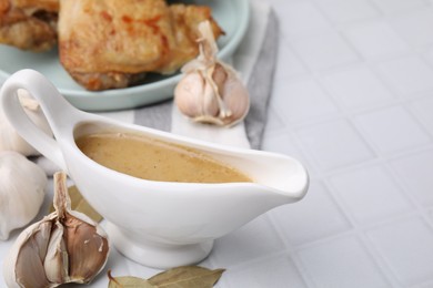 Photo of Delicious turkey gravy in sauce boat on white tiled table, closeup