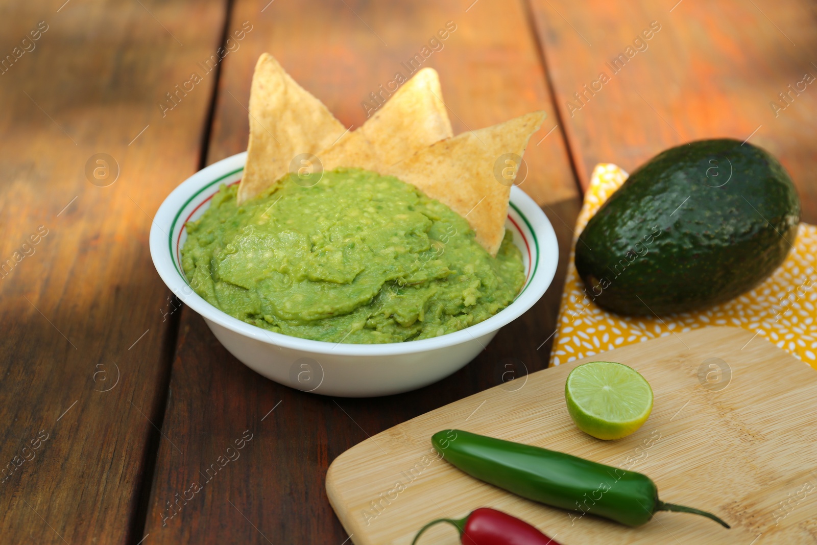 Photo of Delicious guacamole made of avocados with nachos and peppers on wooden table