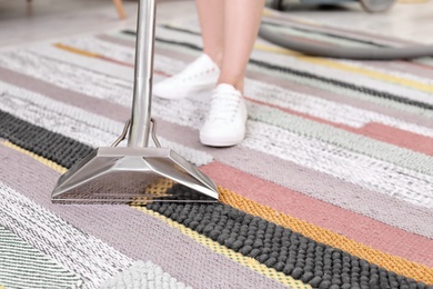 Female worker removing dirt from carpet with professional vacuum cleaner indoors