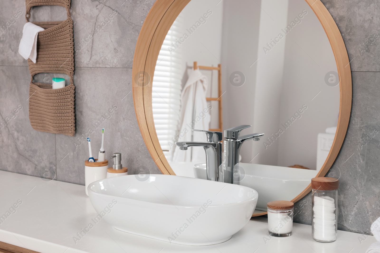 Photo of White vessel sink, mirror and different personal care products on bathroom counter. Interior design